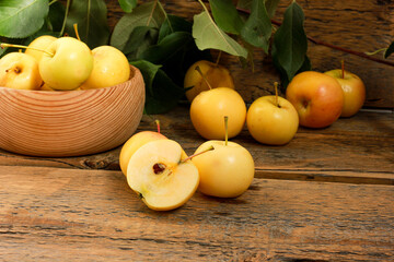 Yellow apples whole and cut into two halves with a knife, on a wooden table among the leaves. Juicy fruit for a vitamin diet and for making for the winter.