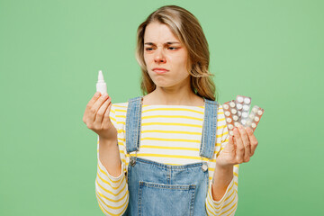 Wall Mural - Sick unhealthy ill allergic woman has red watery eyes runny stuffy sore nose suffering from allergy trigger symptom hay fever hold nasal drops pills isolated on plain green background studio portrait.