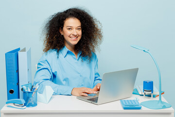 Young smiling fun cheerful successful employee IT business woman wearing casual shirt sit work at white office desk with pc laptop look camera isolated on plain pastel blue background studio portrait.
