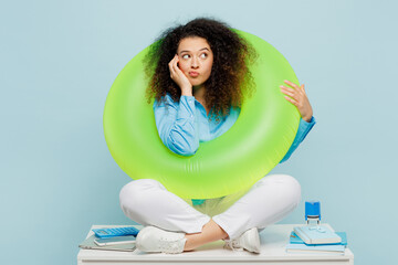 Full body young employee business woman wear casual shirt sit work at white office desk dream about free time vacations hold inflatable ring isolated on plain pastel blue background studio portrait.