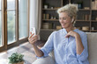 © fizkes - Cheerful elder mature woman talking on video conference call at home, using small wireless earphone in ear, holding smartphone, enjoying smiling, laughing, enjoying online conversation