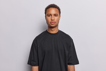Portrait Of Serious Dark Skinned Young Man Looks With Calm Self Confident Expression Has Determined Look Wears Casual Black T Shirt Isolated Over White Background Listens Important Information