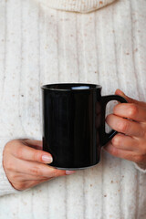 Closeup of girl holding blank black coffee mug mockup. Dark mug mock up for your company logo and design.