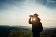 © Kate Stock - A young adult female hiker and traveler looks through binoculars in the mountains in the magical evening light of a sunset