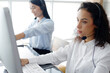 Smiling Caucasian and Asian women call center or secretary operator with headset and microphone is thinking and consultant to customers. Technician Support staff for advise technical issues teamwork.