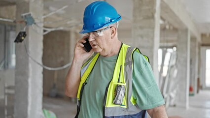 Poster - Middle age grey-haired man builder talking on smartphone with relaxed expression at construction site