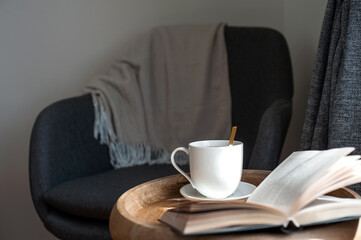 Armchair warm blanket opened book with teacup on wooden table