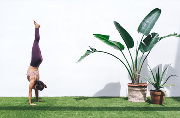 Wall Mural - Female in tracksuit doing sportive exercise for feeling body muscles during pilates workout at terrace with decorative plant, fit girl stretching during physical hatha retreat and active training