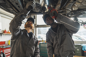 Two car service workes repairing vehicle chassis, standing under it. High quality photo