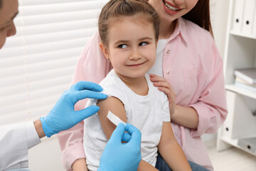 Poster - Children's hepatitis vaccination. Mother with her daughter in clinic. Doctor sticking medical plaster on little girl's arm