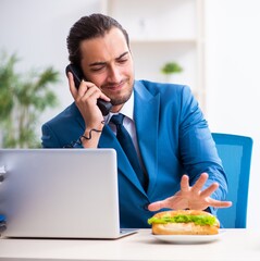 Wall Mural - Young male employee having breakfast at workplace