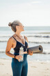 © Westend61 - Woman holding water bottle and exercise mat at beach