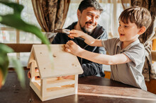 Boy Hammering Nail On Birdhouse By Father At Home