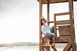 © Westend61 - Smiling woman sitting on lifeguard hut