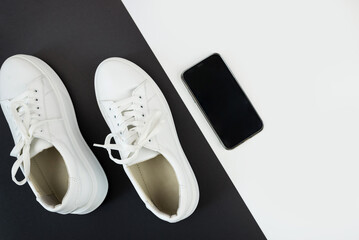 Top view photo of white sneakers with phone and headphones on black and white background