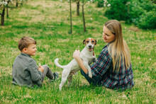 Happy Mother And Son Sitting With Jack Russell Terrier Dog In Garden