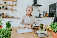 Mature Woman With Tablet PC In Kitchen At Home