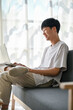 © bongkarn - Side view, A happy young Asian man is watching videos on social media on his laptop