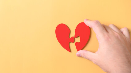 Wall Mural - Hand hold two pieces red heart jigsaw puzzle on yellow background. Health care love wellbeing organ donation family insurance concept. World health day heart day theme. Mental health day praying life