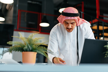 Poster - Young muslim businessman in traditional outfit working at the table in office