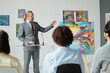 © pressmaster - Gallery owner pointing at modern art on canvas and presenting it to group of people in art gallery