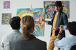 © pressmaster - Artist in elegant clothing presenting his picture on canvas to group of people during exhibition in art gallery