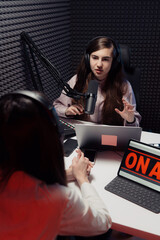 Young woman with headphones talking with guest during radio broadcast in recording studio