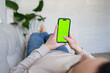 © Julija - Young man at home resting on a couch using with green mock-up screen smartphone. Guy using chroma key mobile phone, internet browsing, posting on social networks.