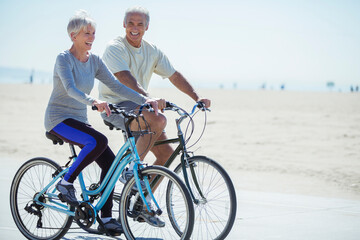 Senior couple riding bicycles on beach boardwalk