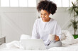 © JenkoAtaman - happy young african american woman relaxing with laptop at home lying in bed  .