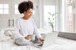 © JenkoAtaman - happy young african american woman relaxing with laptop at home lying in bed  .