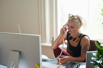 Wall Mural - Young woman headphones tattoo drinking tea talking on telephone in home office