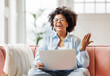 © JenkoAtaman - beautiful young smiling ethnic woman with curly hair uses laptop smiling, gesticulating and talking to online while sitting on sofa