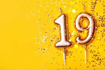 Gold candles in the form of number nineteen on yellow background with confetti. 19 years celebration. Greeting banner.