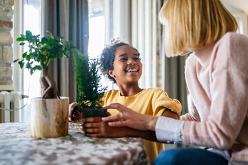 Wall Mural - happy caucasian mother and her adopted african american daughter taking care of plants indoors.