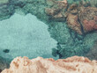 Rocky seabed with blue water and white sand, vertical top view. Mediterranean Sea coast. Lagre stones in the water.