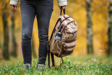 Wall Mural - female hiker holding backpack in hand. woman trekking in autumn forest. adventure in nature
