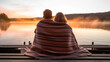 A couple wrapped in a warm blanket, sitting on a wooden dock by a lake, enjoying a serene sunrise