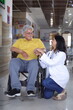 Senior Indian male patient sitting in wheelchair in hospital corridor with female nurse doctor.