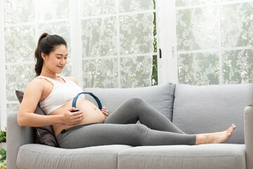 Young Attractive Asian pregnant woman listen music and lying on bed.Pregnant woman use headphones to play classical music for baby in belly learn and Development feeling so relax,Pregnancy Concept