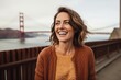 © Anne Schaum - Lifestyle portrait photography of a grinning woman in her 30s that is wearing a chic cardigan at the Golden Gate Bridge in San Francisco USA . Generative AI
