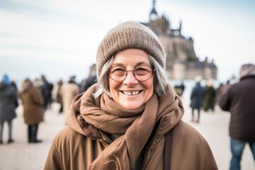 Wall Mural - Portrait of a smiling senior woman with a hat and scarf standing in front of the Notre Dame de Paris