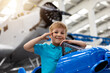 © Kirill Gorlov - Portrait of cute little blond happy kid boy enjoy have fun play riding pedat toz plane model against vintage airplane background in museum hangar. Future child profession dream concept