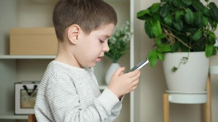 Wall Mural - A preschool boy plays a game on a smartphone, runs his fingers across the screen and talks