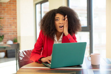 Wall Mural - pretty afro black woman feeling extremely shocked and surprised. businesswoman and laptop concept