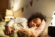 Cute African American little boy sleeping in bed with toy at night