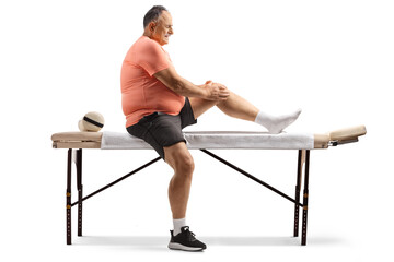 Sticker - Full length profile shot of a man sitting on a massage bed and holding his knee