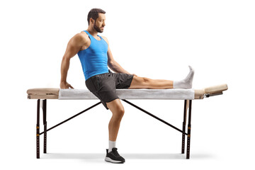 Wall Mural - Male athlete with an injured leg sitting on a massage bed