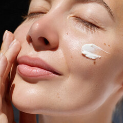 Skincare daily treatment. Beauty close up portrait of young woman with a healthy skin is applying a facial care product. Cream smear.