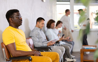 Wall Mural - Middle-aged male patient sitting on the bench in waiting room of clinic together with other guys